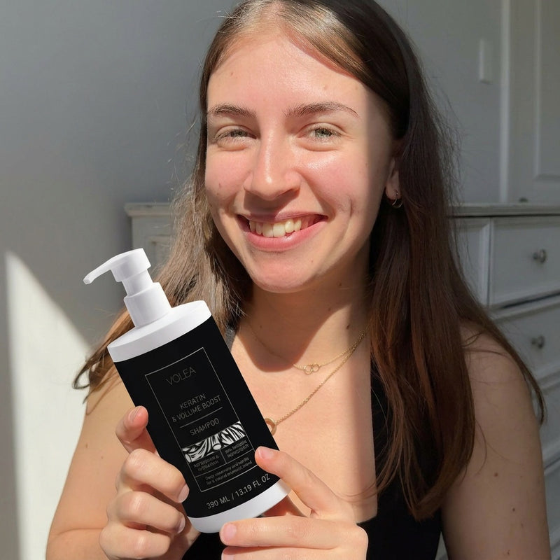 Woman holding a black and white bottle with a pump, smiling indoors.