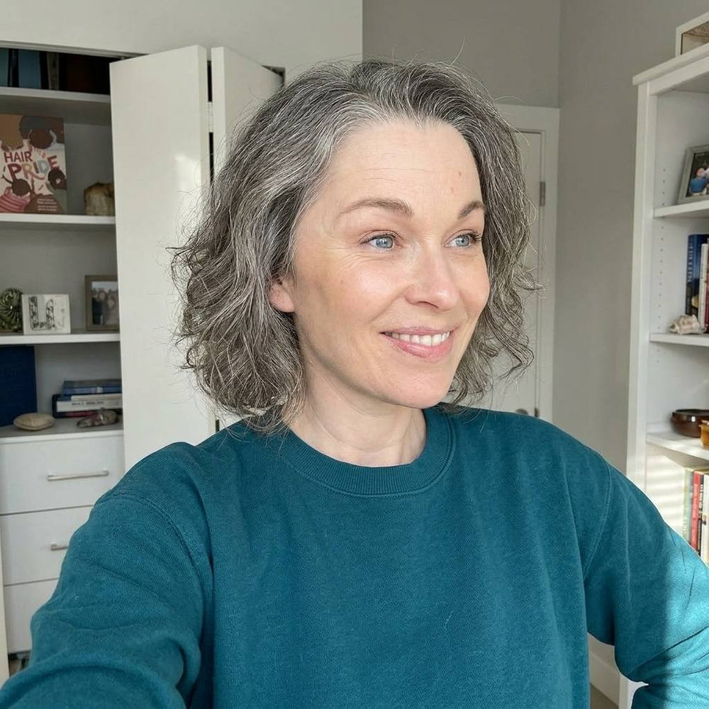 Woman with gray hair wearing a teal sweater in a room with shelves and books.