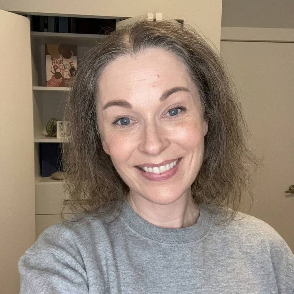 Woman with shoulder-length brown hair wearing a gray sweater indoors.